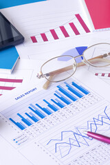 Business graphs, charts, data tables, sales report, pen, glasses, smartphone.