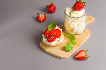 Sandwich with cheese, fresh strawberries and basil on a wooden board and a jar of ricotta. Close-up, on a gray background, horizontal with space