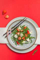 Salad with arugula, strawberries, ricotta and chia seeds, with wooden chopsticks. Overhead, on a bright red background, a copy of the space,vertical