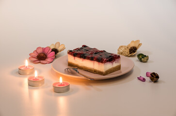 Slice of cheesecake with Raspberry and Currant sauce in a pink plate, with romantic candles set, closeup view. Fruit sauce poured on cheesecake