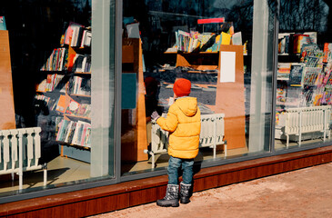 boy examines the window of a bookstore on the street..