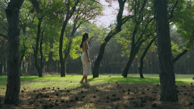 a girl in a white dress walks in the woods