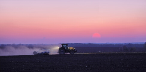 In spring tractor plows in field on background of sunset.