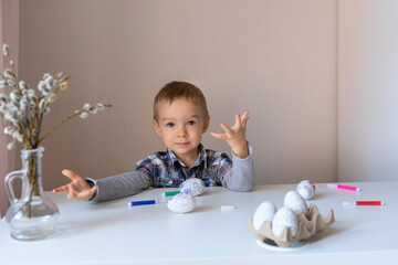 The kid got his fingers dirty. A little boy is engaged in creative work at home at the table. Preparation for the Easter holiday. Willow twigs decorate the table.Home classes for the child.