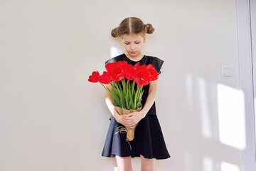 Sad child girl with a bouquet of red tulips in black dress