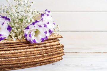 Matzah and flowers for Jewish holiday Pesach on white wooden background with copy space.