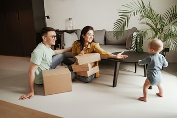 Happy couple is playing with baby and smiling at home. Young family moving to new apartment