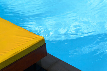 Poolside wooden bed with yellow cushions.