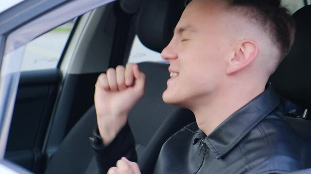 Young man singing and dancing while sitting in the car. Side view of male driver dancing with hands