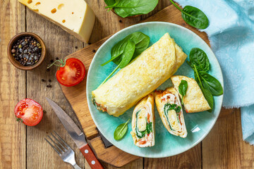 Japanese cuisine. National Japanese dish Omelet tamago yaki for breakfast. Rolled egg with spinach, tomato and cheese on a wooden table. Top view, flat lay.