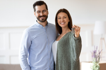 Portrait of overjoyed Caucasian young couple renters show keys to new house excited moving in...
