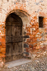  Ricetto di Candelo. Antica porta in legno, con edera rampicante sul muro, in mattoni rossi. Villaggio medievale a Biella, Piemonte, Italia
