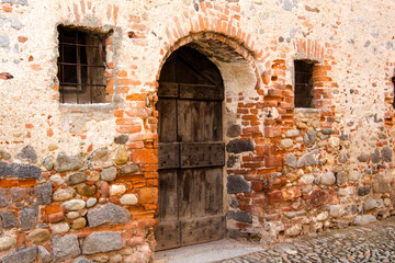 Fototapeta na wymiar Ricetto di Candelo. Antica porta in legno, con edera rampicante sul muro, in mattoni rossi. Villaggio medievale a Biella, Piemonte, Italia 