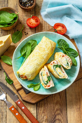 Japanese cuisine. National Japanese dish Omelet tamago yaki for breakfast. Rolled egg with spinach, tomato and cheese on a wooden table. Copy space.