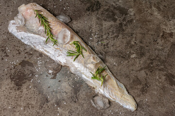 Raw frozen hake fillet with ice and fresh rosemary