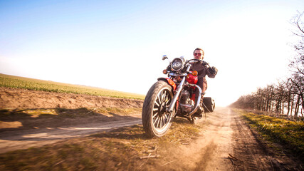 Fototapeta na wymiar Guy in leather jacket riding through the fields off-road countryside on chopper in autumn sunny day,