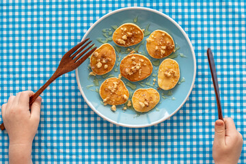 Miniature pancakes with honey and walnuts on blue background. Food for kids.