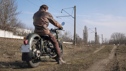 Long shot of hot biker wear leather jacket on vintage motorcycle prepares to ride a dirt road...