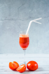 Freshly squeezed tomato juice in a glass on a blue and summer background. Vegetable cocktail with plastic tubes on the table. Empty space for text