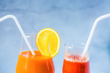 Close up freshly squeezed strawberry and orange juice in a glass on a blue and summer background. Fruit cocktails with plastic tubes on the table. Empty space for text