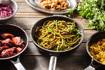 Dark pans with various food such as spaghetti pesto, risotto, and glazed chicken wings