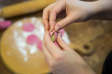 Dumplings in flour on a wooden board, hands sculpt a dumpling before cooking. Top view, close up.
