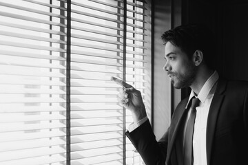 portrait of young middle east handsome businessman wearing suit and tie, standing near window in office. business concept (black and white monochrome)