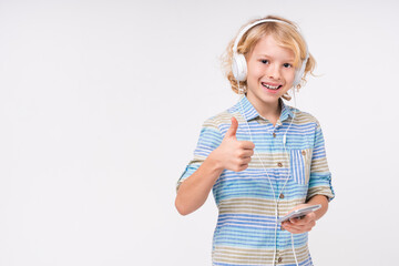 Excited caucasian preteen boy listening to the music and using phone with thumb up isolated over white background