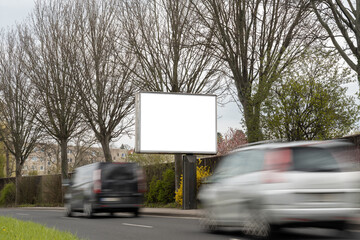 Advertisement billboard panel for a mockup. Empty template for an ad next to a street with moving cars. Space for a commercial poster in the inner city. White display in a public area.