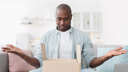 Home delivery. Shocked african american man spreading his hands, having problem, getting wrong order or empty box