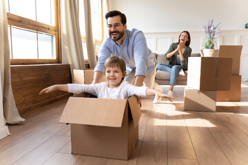 Happy young Caucasian family with small son have fun on relocation day to new house or apartment. Smiling man and woman enjoy unpacking with little child moving to own home. Rent, mortgage concept.