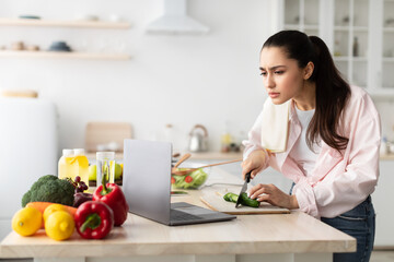 Woman cooking salad and using laptop and kitchen