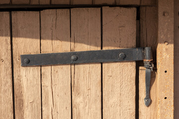 Old black crooked hinge with ancient nails. Old brown wood planks