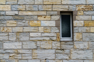 Fototapeta premium A fragment of a gray stone wall with window made of hewn stone of a rectangular shape.