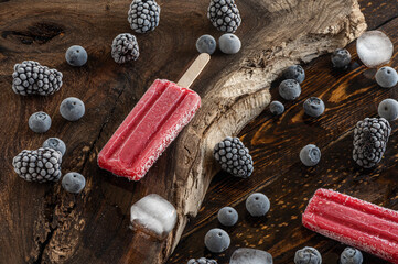 Fototapeta na wymiar Frozen blackberries, blueberries, ice lollies and ice cubes over a wooden board