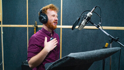 Expressive bearded man with curly ginger hair in headphones at recording studio stay opposite a...