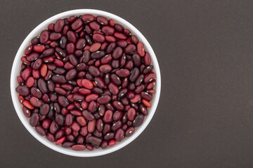 Beans in a white glass bowl. Top view photo of kidney red beans on dark grey background.