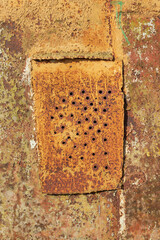 Yellow rusted metal sheet with holes and welded patch.