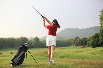 Beautiful golf course at the sunset, sunrise time,female golf player on professional golf course. Golfer with golf club taking a shot