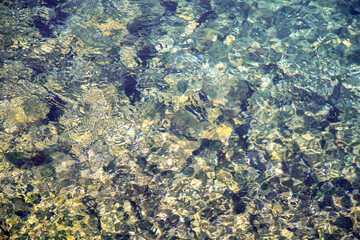 The pebbles at the bottom of the stream shine through and shimmer with light at the bottom of the stream with crystal clear water. Texture. Transparent. Background. Abstract
