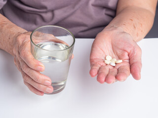 Senior woman with pills and glass of water at home. Close-up photo. Aged people and healthcare concept