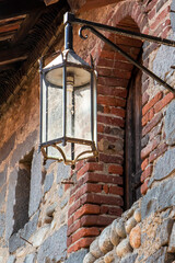 Ricetto di Candelo. Antico lampione di casa medievale con muro in pietra e mattoni rossi. Villaggio...