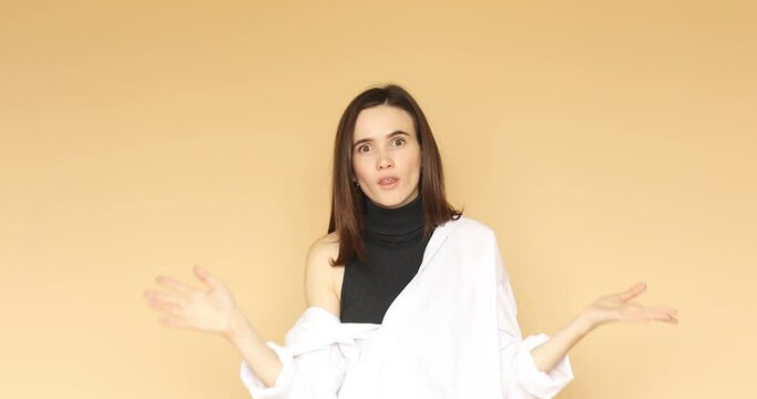 Portrait of woman shushing with finger on lips gesture, asking to keep silence and shrugs her arms with angry serious expression, isolated on beige background, mysterious confidential information.