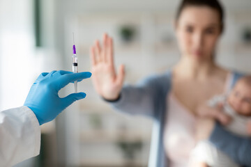 Vaccine Hesitancy. Woman With Newborn Baby Refusing Syringe In Doctor's Hand - obrazy, fototapety, plakaty