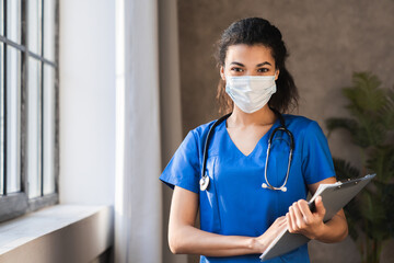 Confident young female african scrub nurse wear blue uniform, face mask,standing arms crossed in hospital hallway. Black millennial woman doctor, surgeon, medic staff professional portrait. - Powered by Adobe
