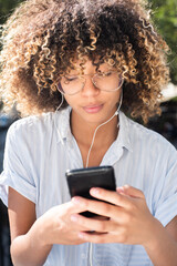 Close up young African American woman listening to music with earphones and mobile phone