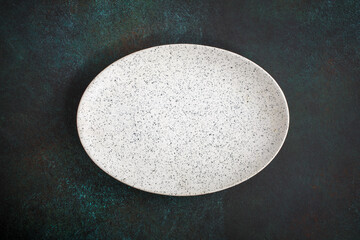 Empty oval plate on dark concrete background. Top view, with copy space
