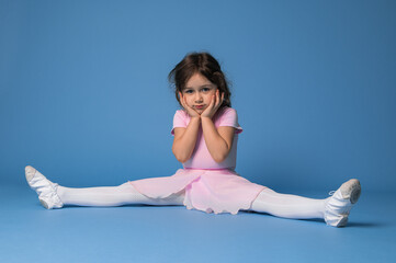 Cute ballerina in pink dress perfecting twine while sitting on blue background