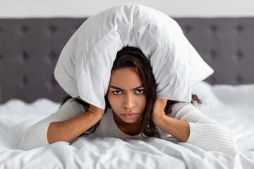 Stressed angry black woman covering ears lying in bed
