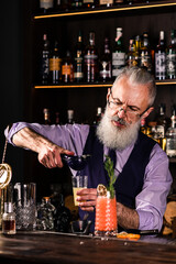 Stylish brutal barman makes a cocktail at bar counter background